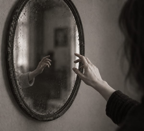 Ghosting – plötzlich ist der geliebte Mensch verschwunden Eine Hand streckt sich nach einem alten, schmutzigen Spiegel, während eine andere Hand im Spiegel reflektiert wird.
